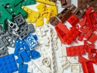 Várias peças de quebra-cabeça de diferentes cores. As peças estão espalhadas em cima de uma superfície branca. Elas sugerem os diferentes casos de como usar o verbo to be.