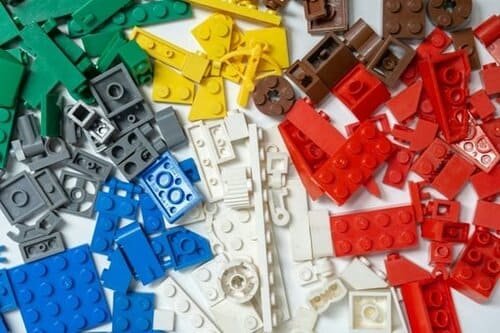 Várias peças de quebra-cabeça de diferentes cores. As peças estão espalhadas em cima de uma superfície branca. Elas sugerem os diferentes casos de como usar o verbo to be.