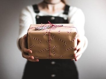 Uma pessoa segurando uma caixa de presentes, como se fosse entregá-la a quem está na sua frente. A imagem sugere a ideia de como usar possessivos em inglês.