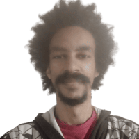 Rapaz de pele negra, de cabelos e barba preta, olhando de frente para a câmera.